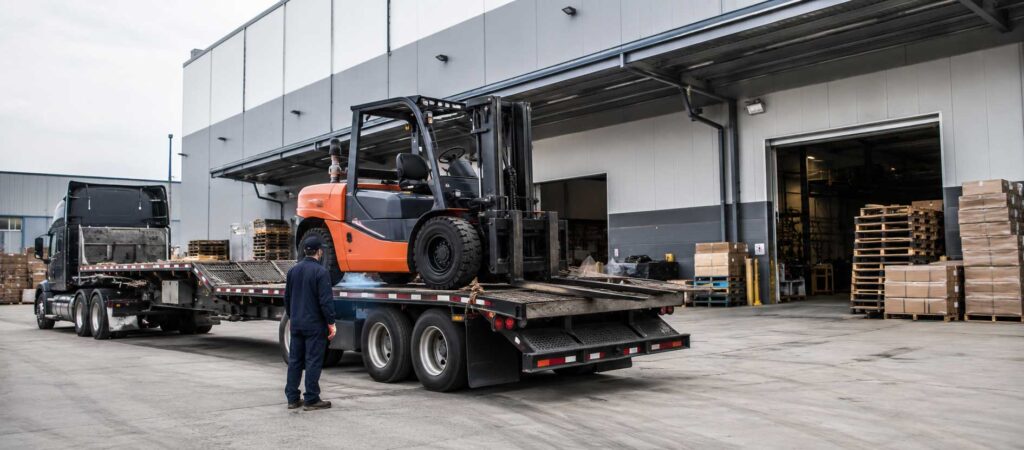 Forklift being safely loaded onto a flatbed tow truck for transport at an industrial warehouse